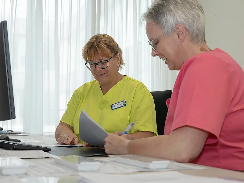 Zwei Pflegekräfte sitzen vor einem Computer und besprechen Medikamentenpläne.