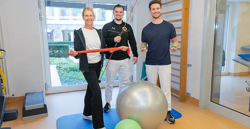 Eine Gruppe von Therapeutinnen und Therapeuten, die verschiedene Trainingsmittel in den Händen halten.