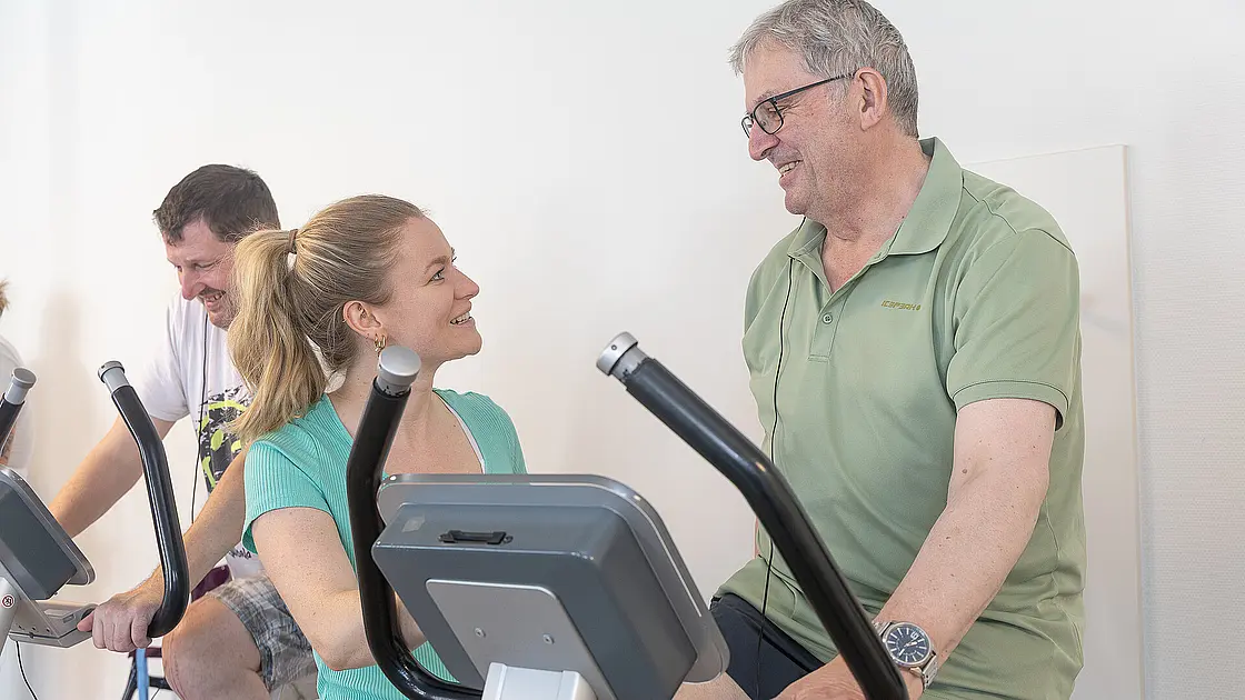 Eine Physiotherapeutin begleitet einen Patienten beim Training an einem Fahrradergometer.