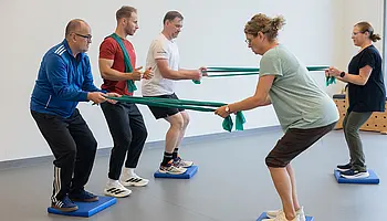 Eine Gruppe von Menschen, die gemeinsam mit dem Therapeuten Übungen mit Terrabändern macht.