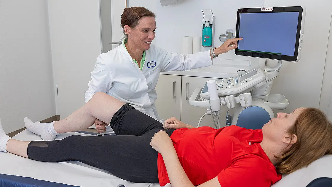 Eine Ärztin untersucht per Ultraschall das Knie einer liegenden Patientin.
