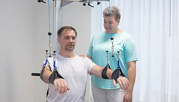 Eine Therapeutin überwacht einen Patienten, der seine Arme am Arm-Schulter-Trainer trainiert.