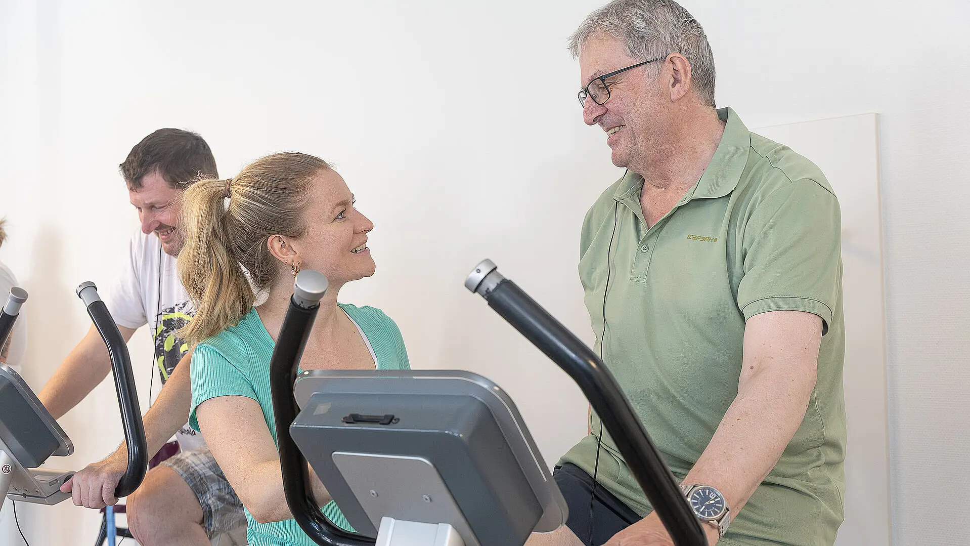 Eine Physiotherapeutin begleitet einen Patienten beim Training an einem Fahrradergometer.