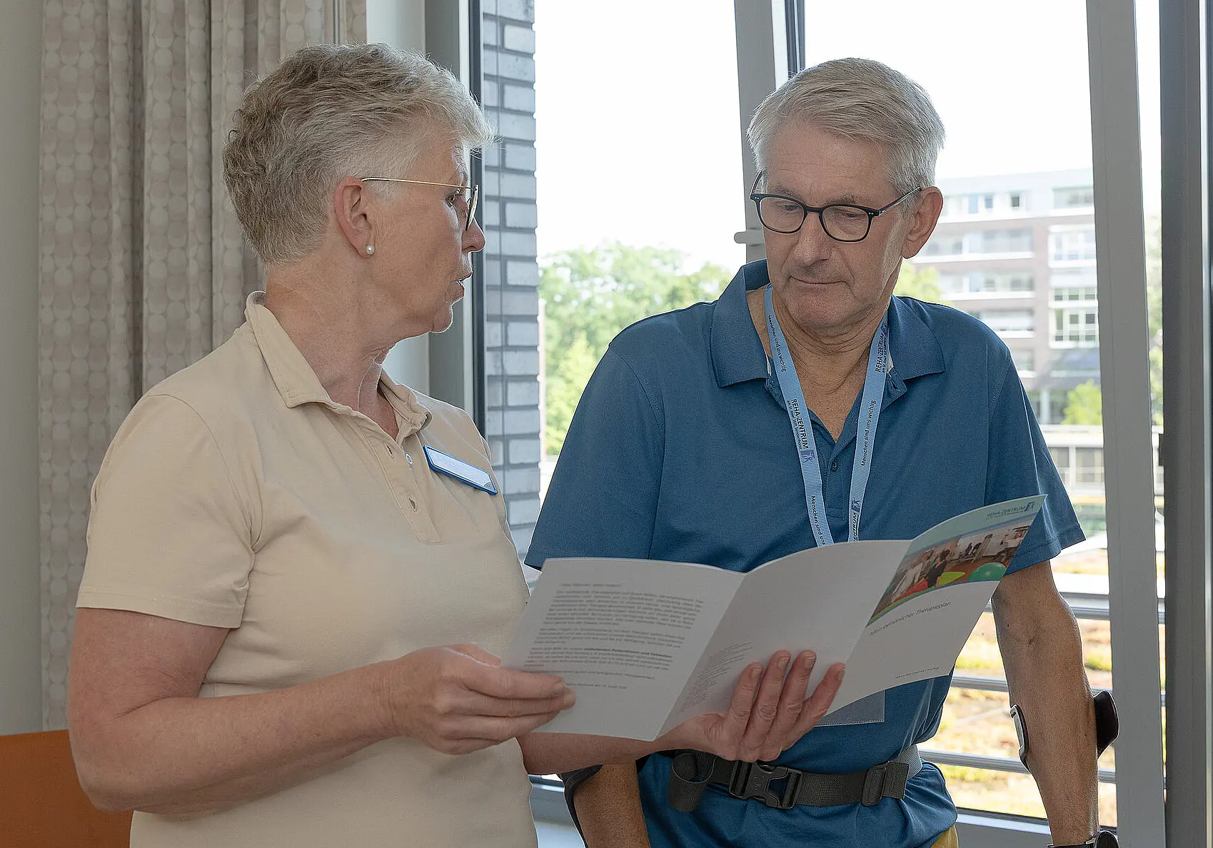 Eine ältere Pflegende erklärt einem Patienten eine Broschüre