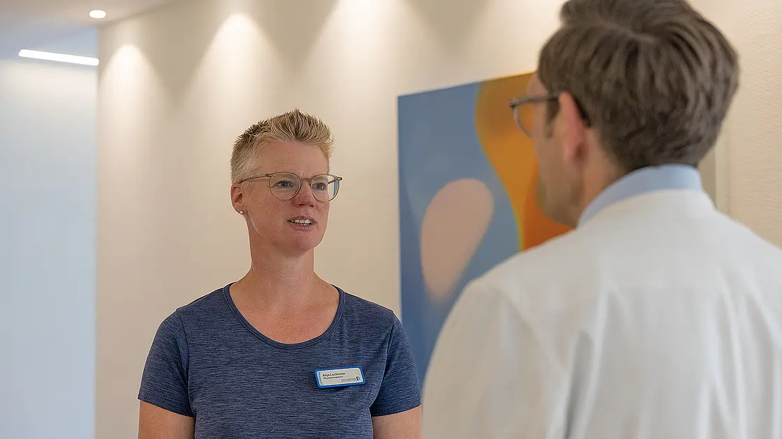 Ein Frau in Sportkleidung spricht mit einem Mann in weißem Arztkittel.
