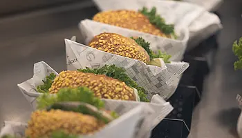 Mehrere belegte Körnerbrötchen mit Salat liegen einzeln angerichtet in Servierkörben.