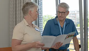 Eine Pflegefachkraft und ein Patient betrachten gemeinsam eine Informationsbroschüre.