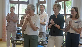Mehrere Gäste und Mitarbeitende stehen in den Räumen des Café Clara und applaudieren während der Wiedereröffnung.