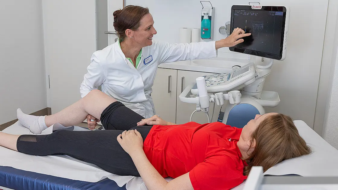 Eine Ärztin untersucht per Ultraschall das Knie einer liegenden Patientin.