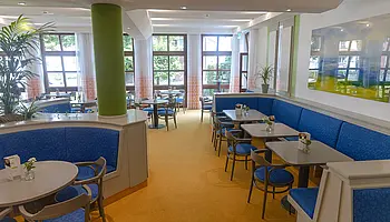 Blick durch den hellen Gastraum des Café Clara mit Sitzgruppen, blauen Polsterbänken und großen Fensterfronten.