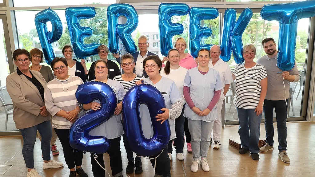 Ein Foto von einer Gruppe von Menschen, die in der Hand Luftballons halte, die das Wort "Perfekt" und die Zahl 20 ergeben.