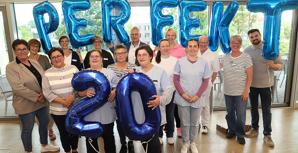 Ein Foto von einer Gruppe von Menschen, die in der Hand Luftballons halte, die das Wort "Perfekt" und die Zahl 20 ergeben.